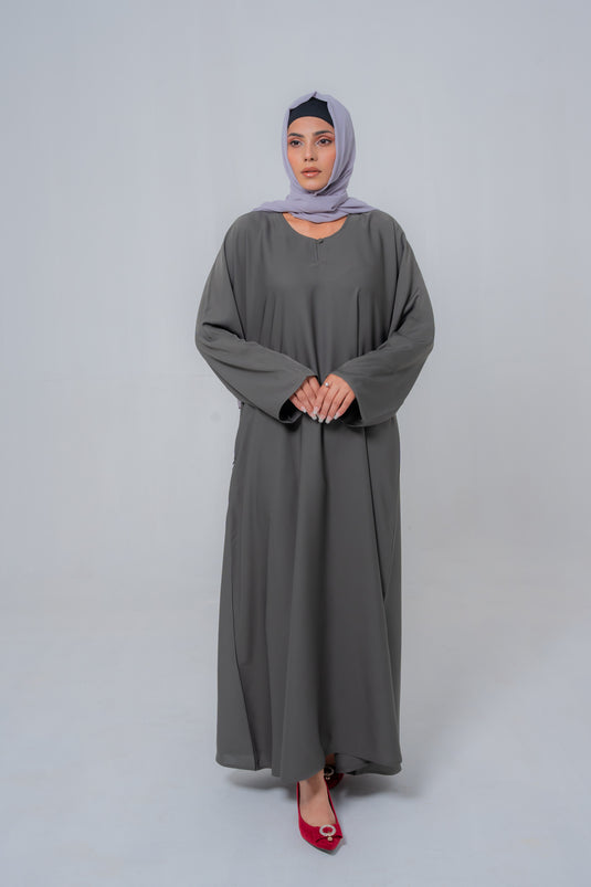 Woman wearing a long gray dress and hijab on a white background