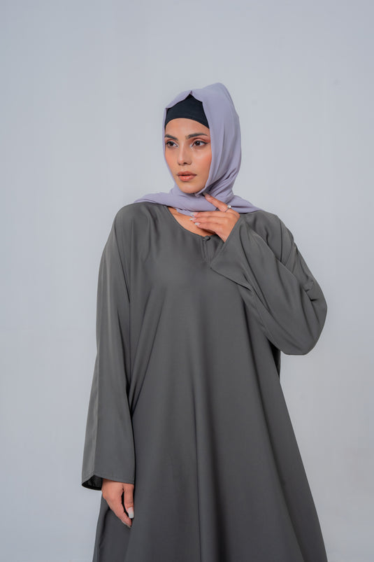 Woman wearing a gray dress and light purple hijab against a plain background