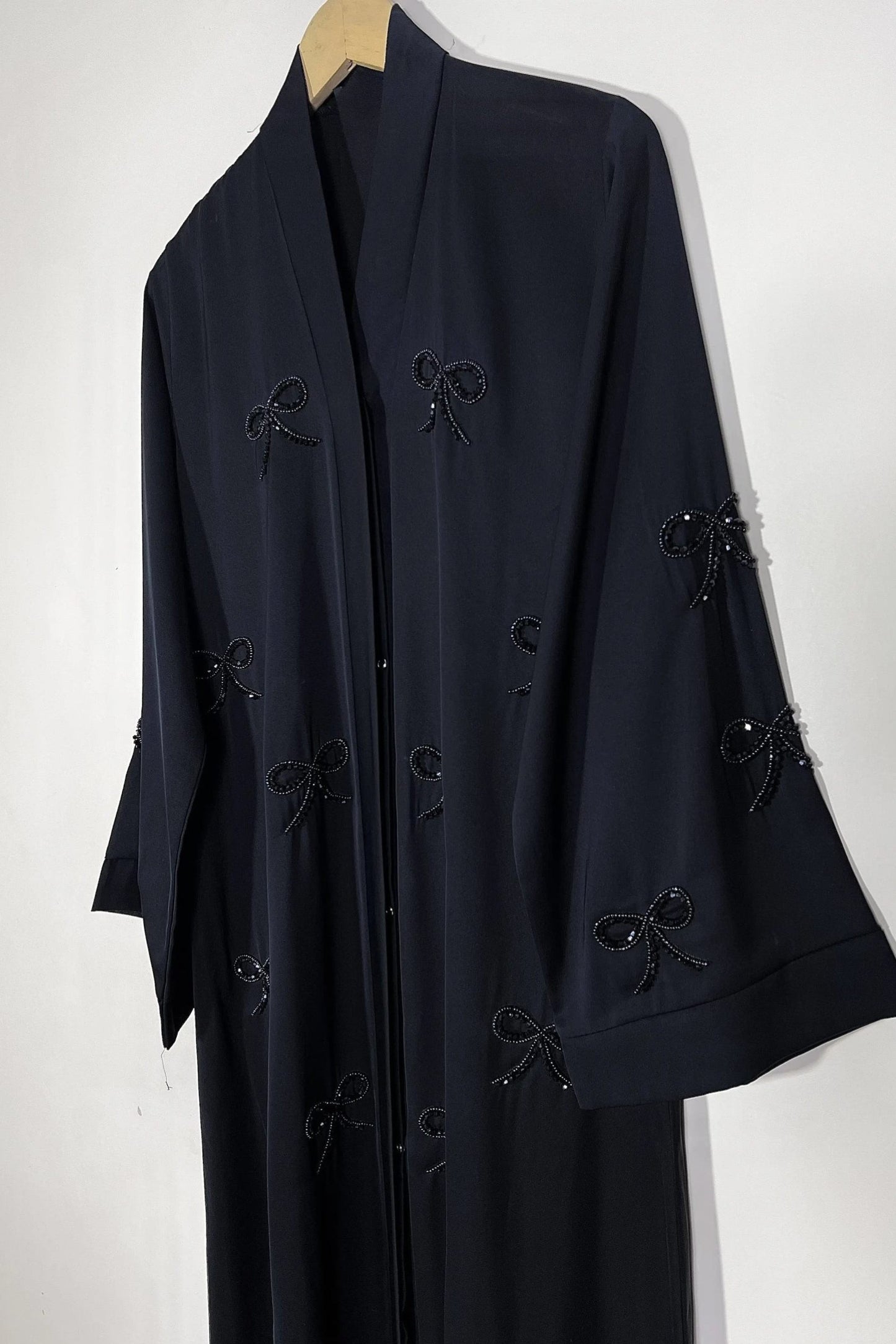 Handworked black premium nida abaya on hanger displaying front open style and elegant bow embellishments