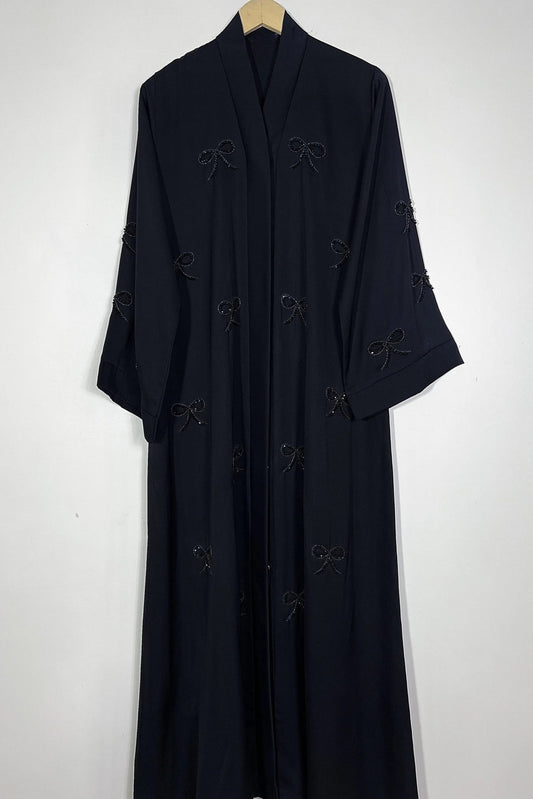 Black Essence of Dreams abaya hanging on hanger showing premium nida fabric and refined handwork bow detailing