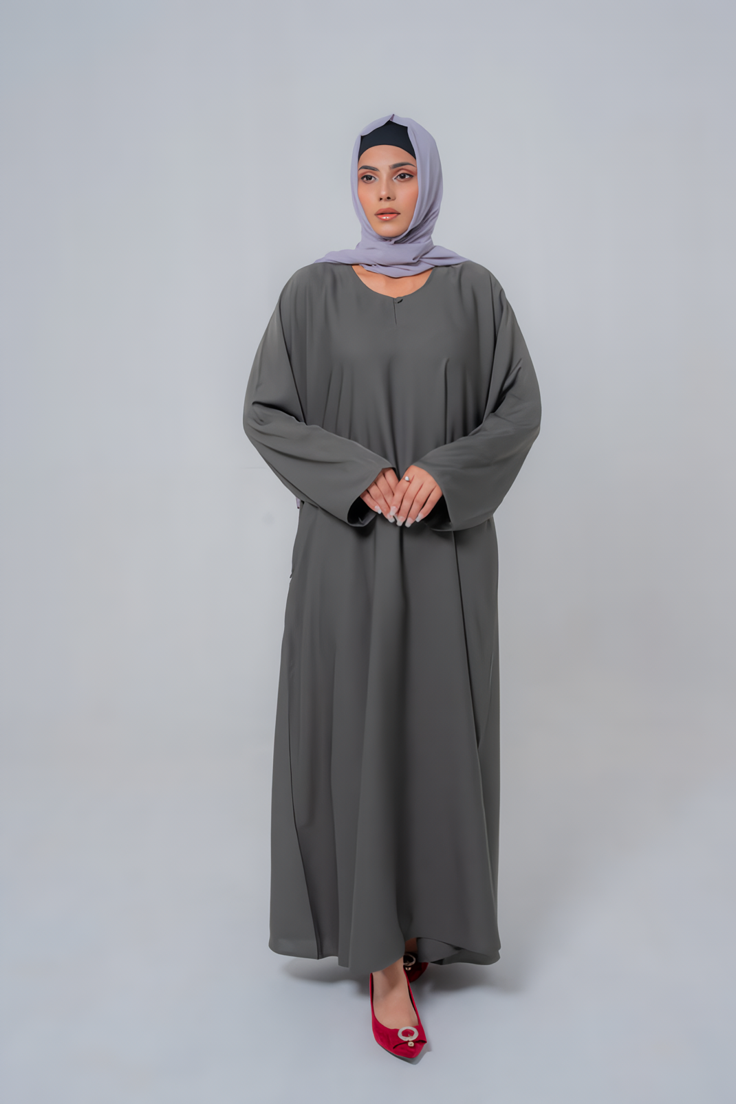 Woman wearing a long gray dress and a matching hijab on a white background.