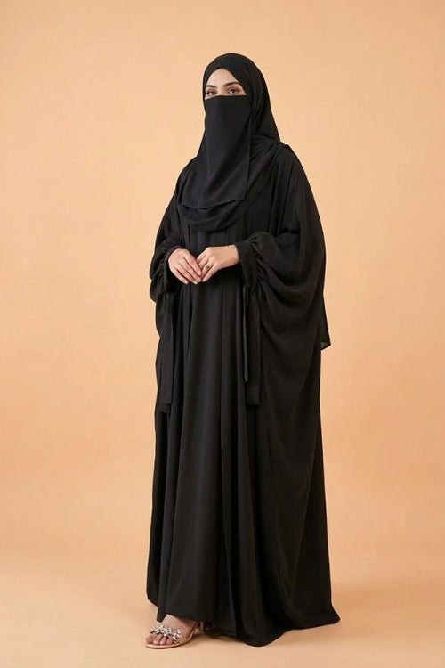 Person wearing a black abaya on a beige background