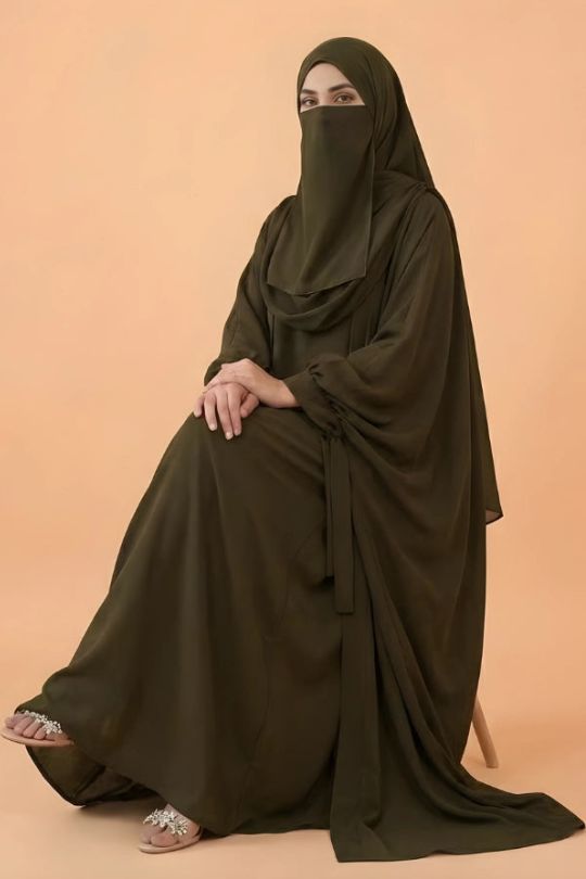 Person wearing a dark green abaya on a beige background