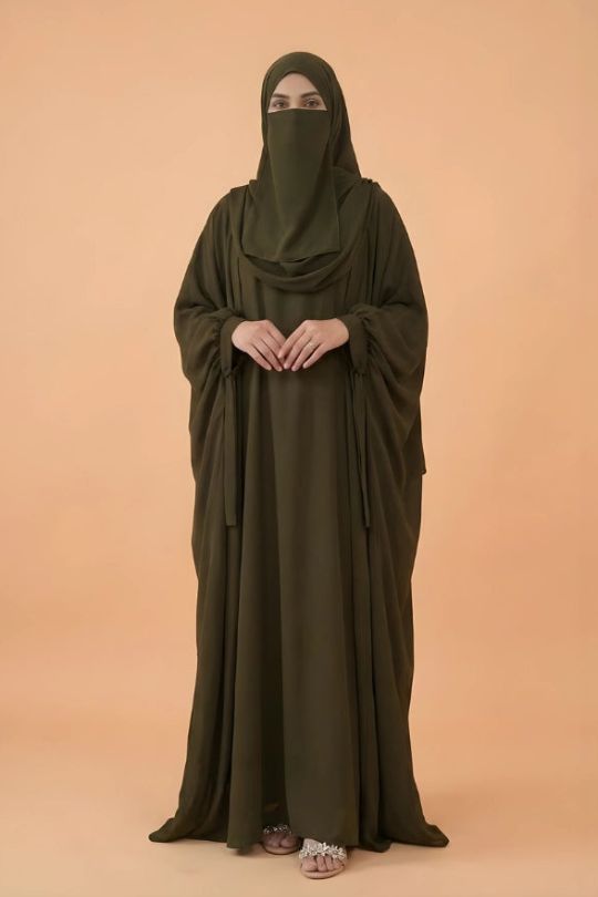 Person wearing a long olive green dress with a matching hijab on a beige background