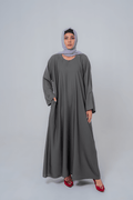 Woman wearing a long gray dress and headscarf on a white background