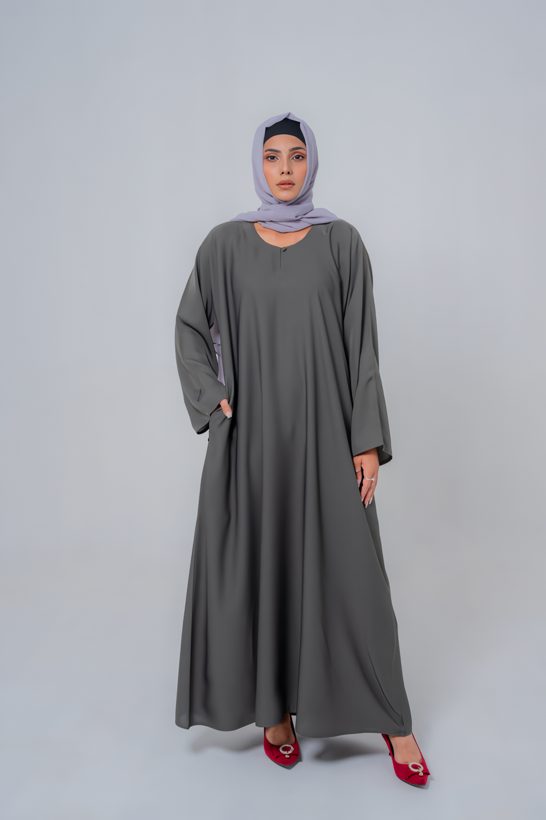 Woman wearing a long gray dress and headscarf on a white background