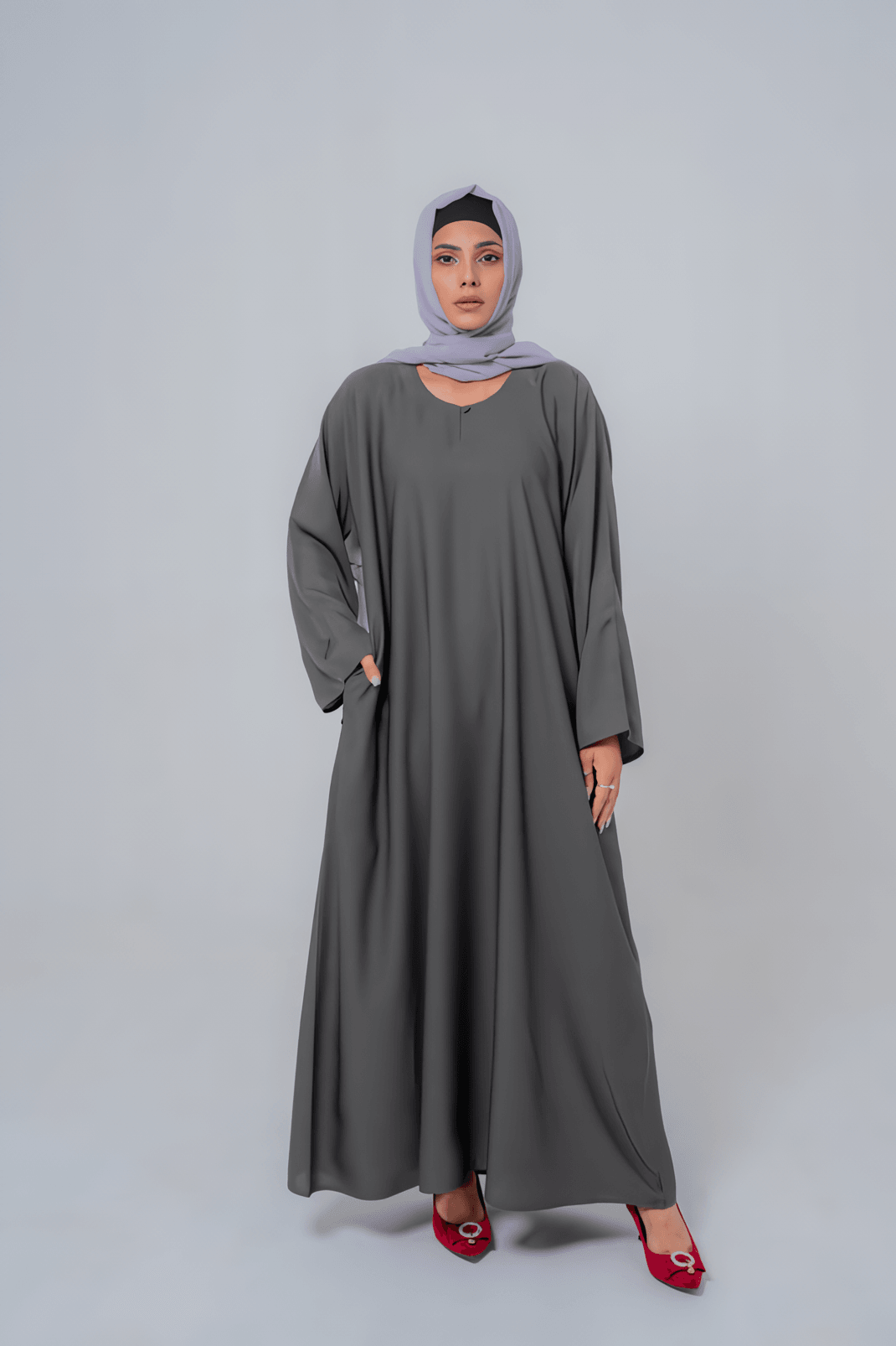 Woman wearing a long gray dress and headscarf on a white background