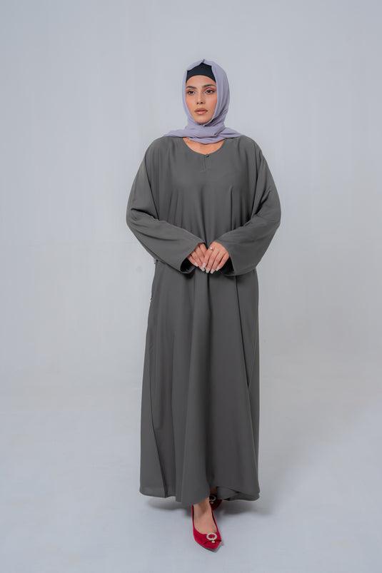Woman wearing a long gray dress and hijab on a white background