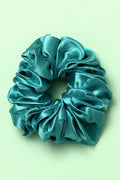 Turquoise satin scrunchie on a light green background