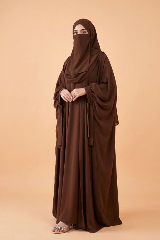 Woman wearing a brown abaya and niqab on a beige background