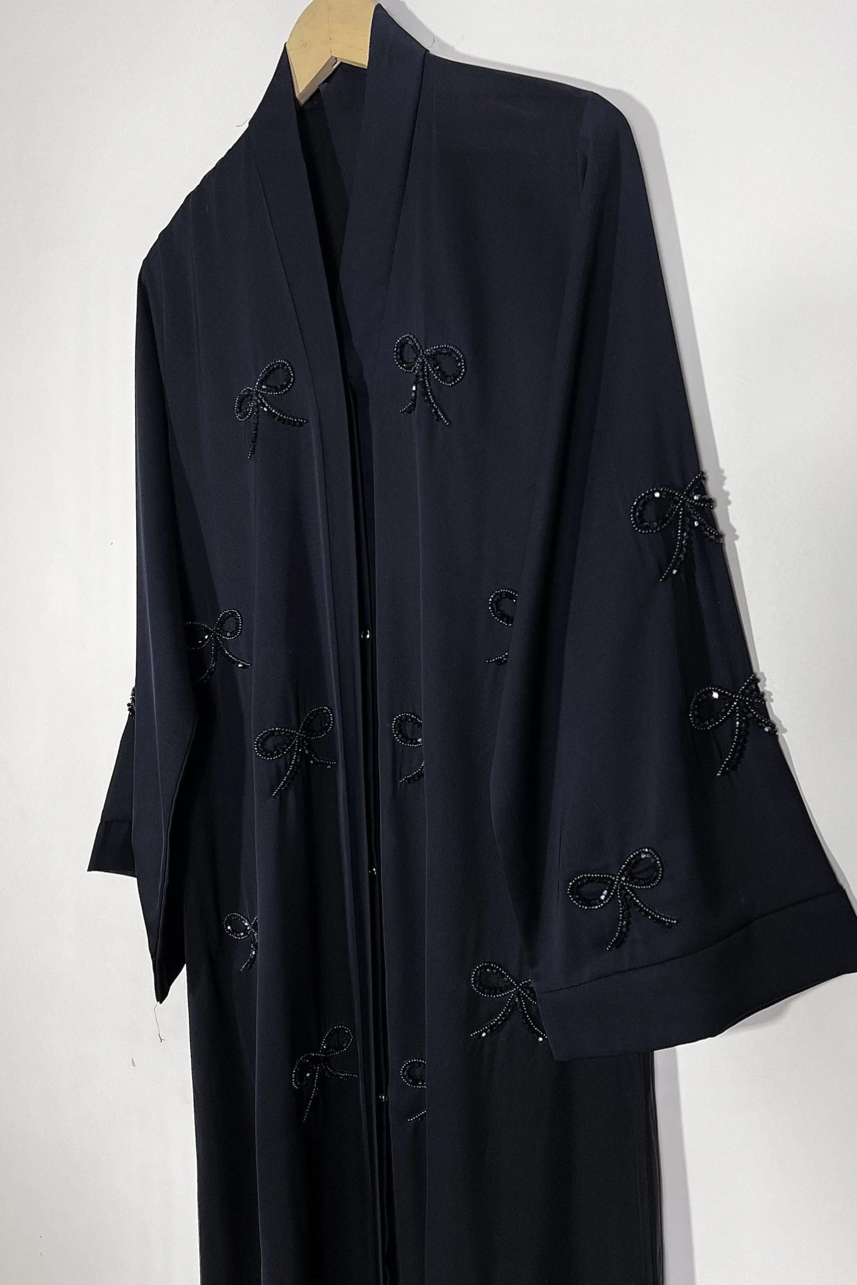 Handworked black premium nida abaya on hanger displaying front open style and elegant bow embellishments