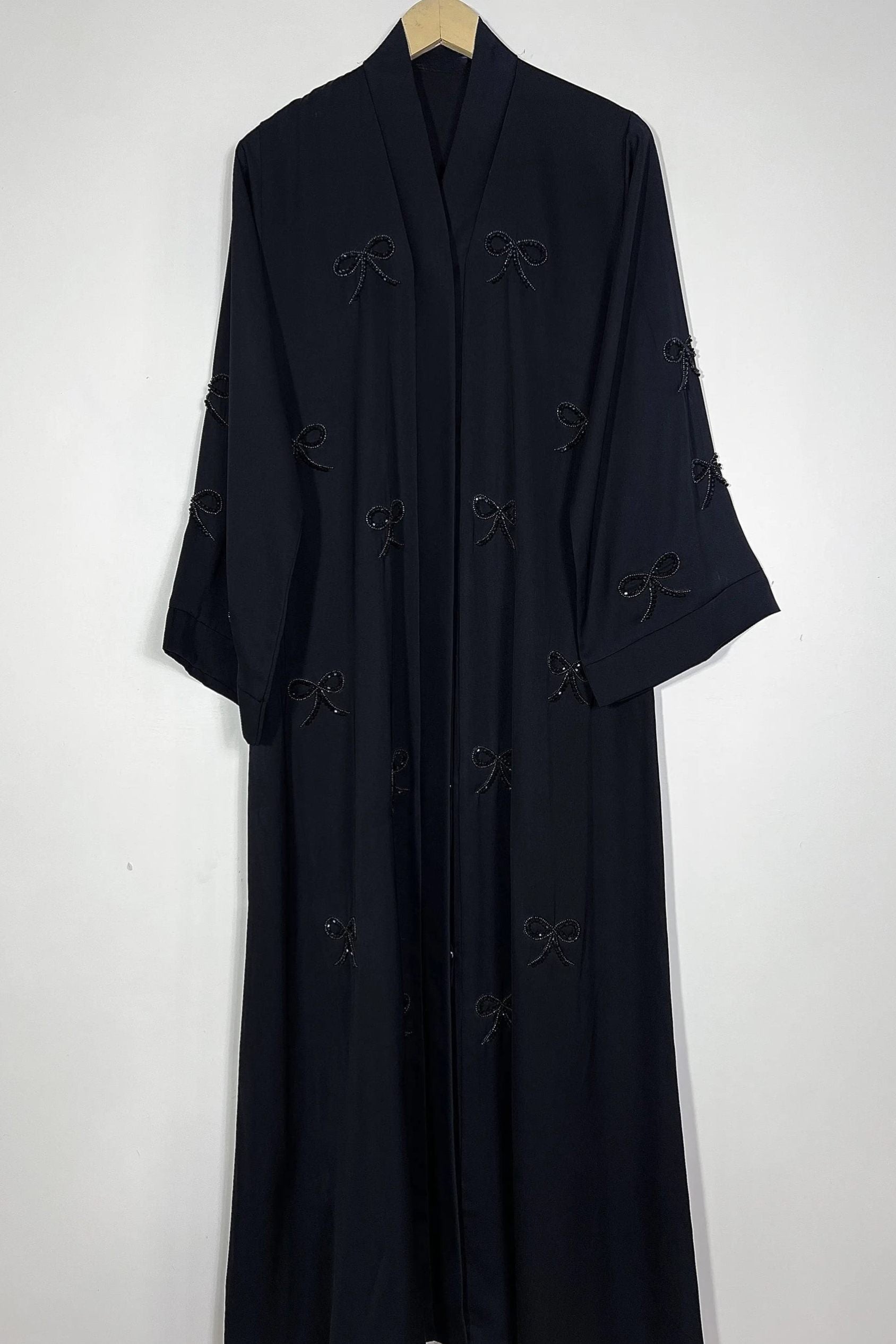 Black Essence of Dreams abaya hanging on hanger showing premium nida fabric and refined handwork bow detailing