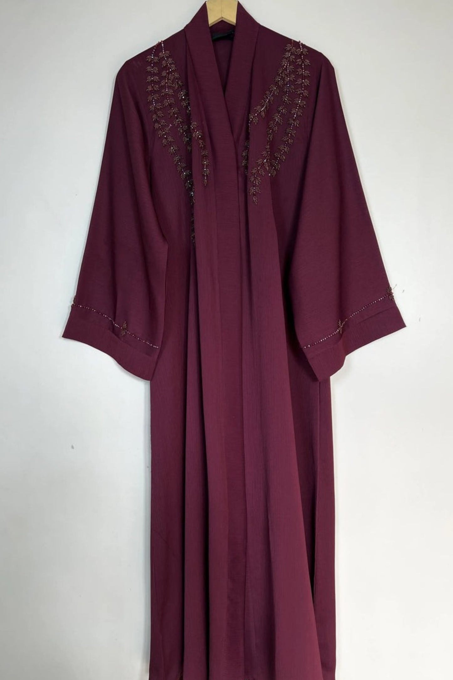 Handcrafted maroon nida abaya on hanger highlighting elegant front open cut and refined bow handwork