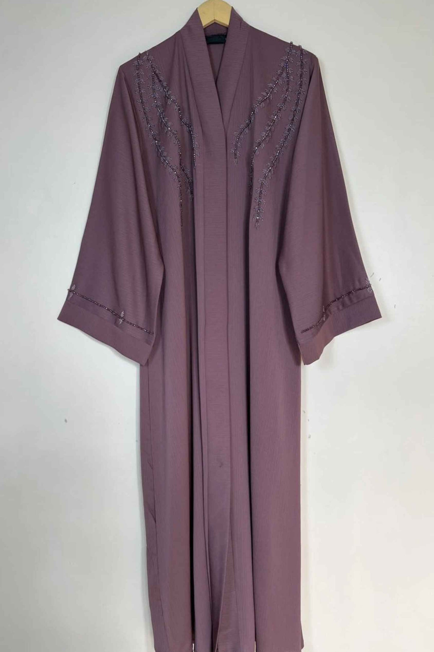 Handworked pinkish nida abaya on hanger highlighting elegant cut and subtle bow embellishments