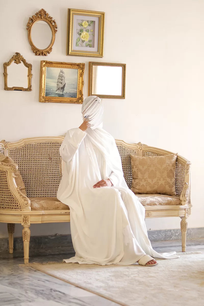 Model wearing premium nida fabric white kaftan sitting on sofa showcasing relaxed fit and elegant indoor styling